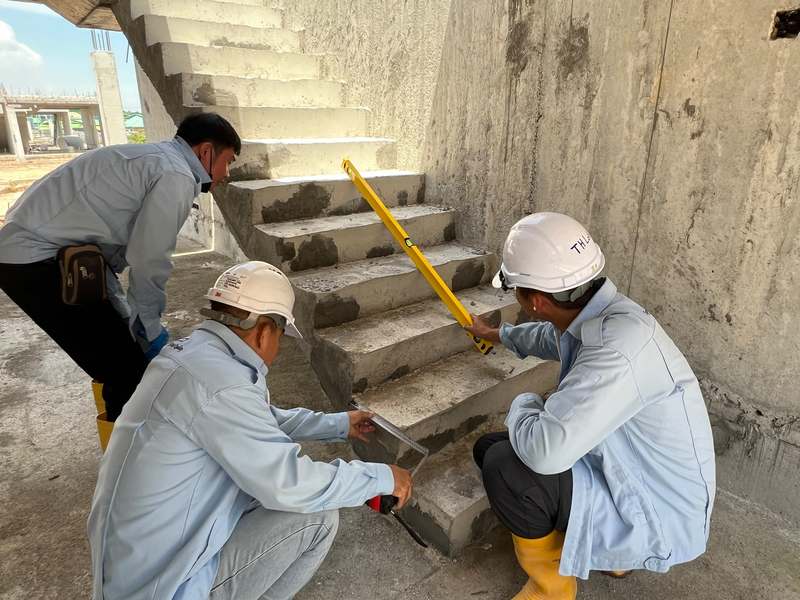 Construction quality inspectors measuring concrete staircase dimensions on an active construction site in Malaysia